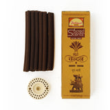 A set of dark brown incense sticks next to their gold-colored packaging box and a white metal incense burner, all on a plain white background. The box features the brand 'Parimal' and the product line 'Sacred Scents'.