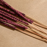 Several dried decorative reed stems with textured green-brown heads and tan stems arranged diagonally on a warm beige surface.