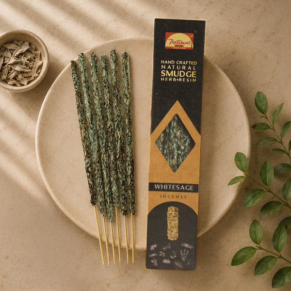 A styled flat-lay of Whitesage Herb resim incense sticks by Parimal. The incense sticks, coated in green herbs, are arranged on a beige ceramic plate next to their black and gold packaging box.